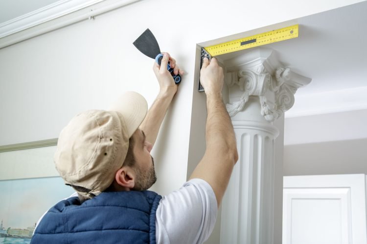 60224688 - worker holds putty knife and measures the wall corner using metal angle. finishing work.
