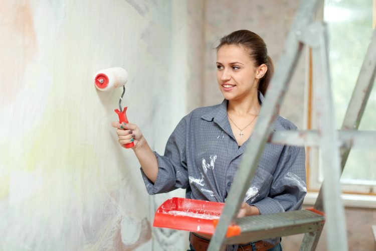 Happy woman paints wall with roller at home